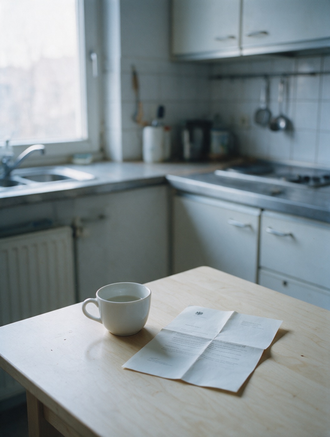Eine halb volle Kaffeetasse neben einem gefalteten Brief auf dem Küchentisch, Stille am Morgen.